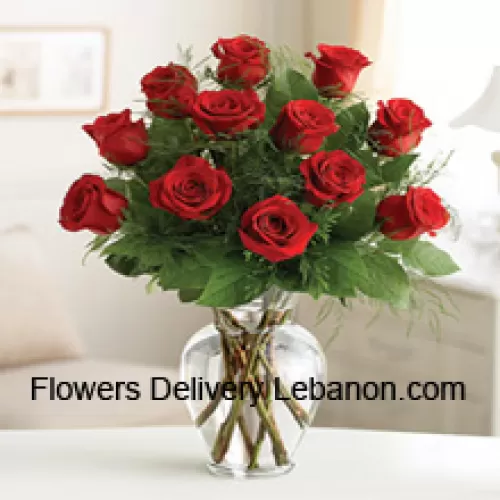 12 punaista ruusua muutamien saniaisten kanssa lasimaljakossa